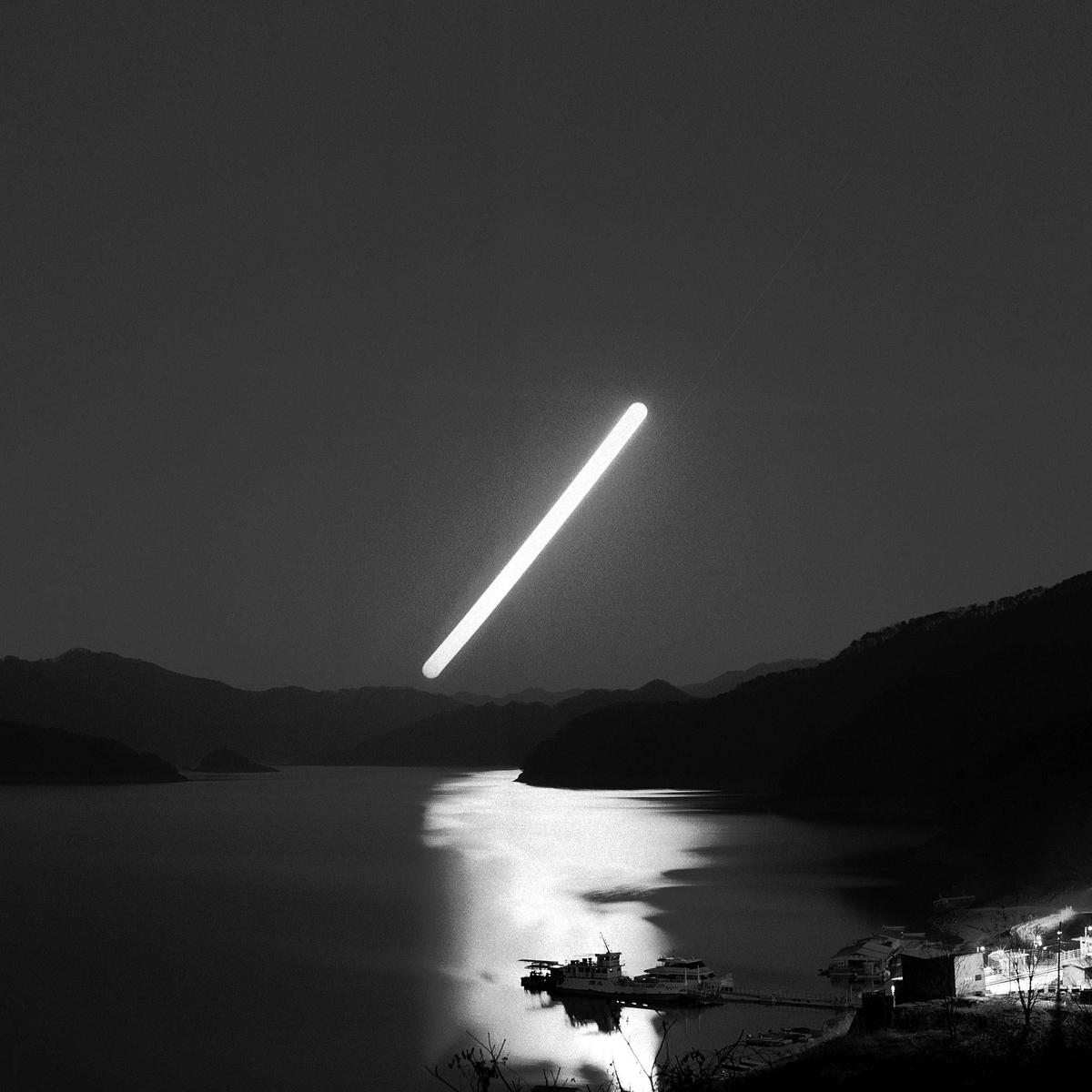 A bright light source illuminates a lake with mountains and a small village at night.
