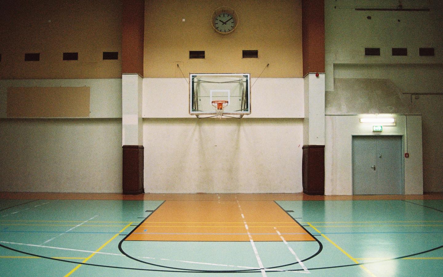 A basketball court with a hoop and a clock on the wall is visible inside a building.