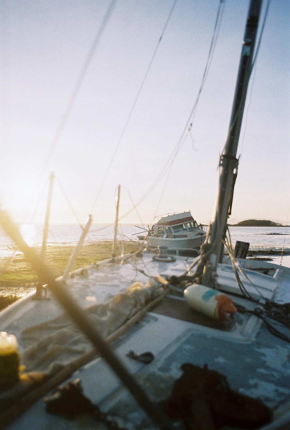 A boat is beached on the shore with another boat visible in the distance under a bright sky.