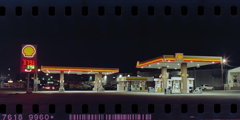 A Shell gas station with a large price sign is illuminated at night.
