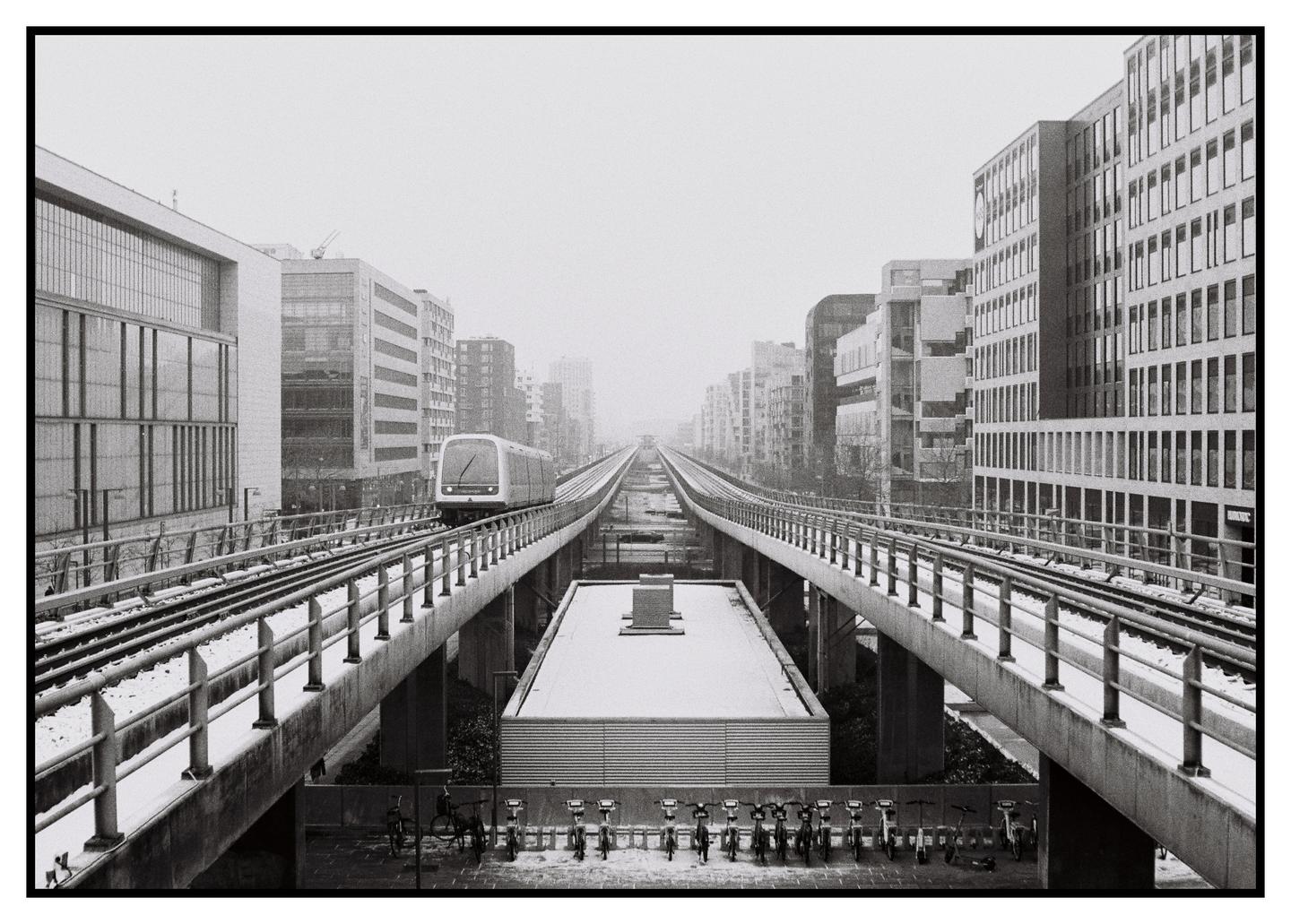 A metro train travels on an elevated track through a city covered in snow.