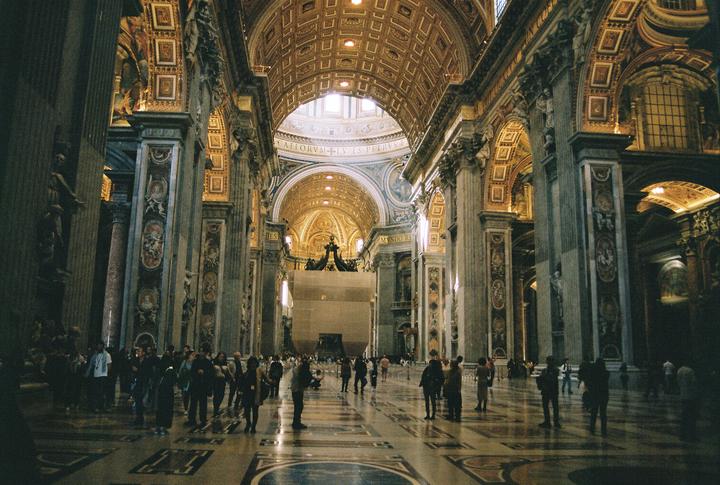 A large crowd of people stands inside a grand, ornate cathedral with a high, domed ceiling.