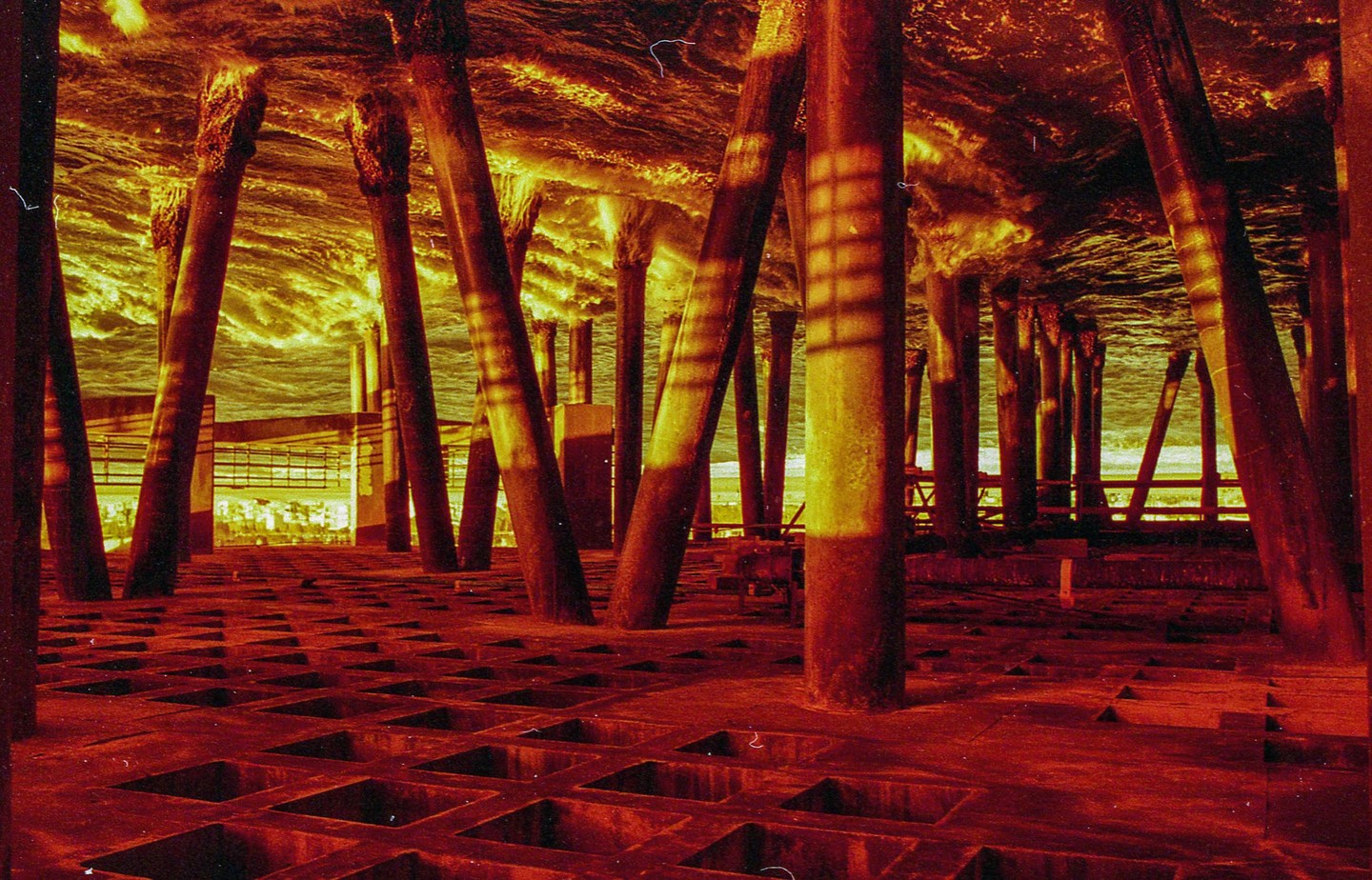 The underside of a pier is visible with waves crashing above and a red-toned floor below.