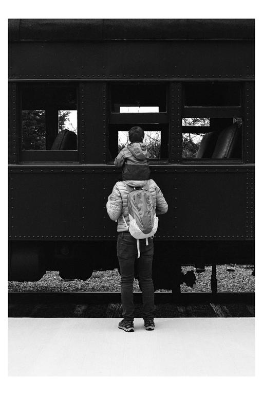 A child sits on a man's shoulders looking into the window of a train car.
