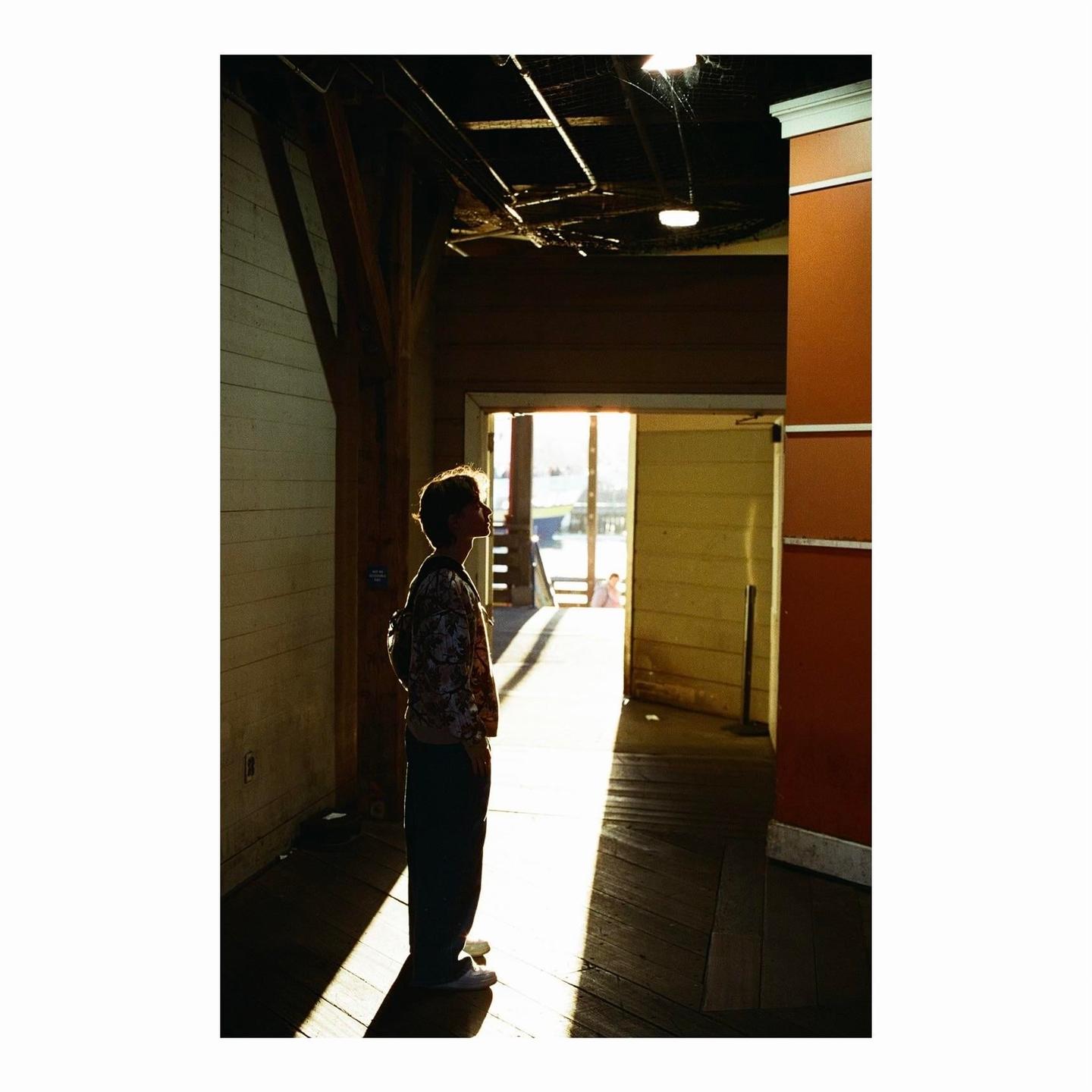 A person stands in a sunlit doorway, looking up, with a backpack on.
