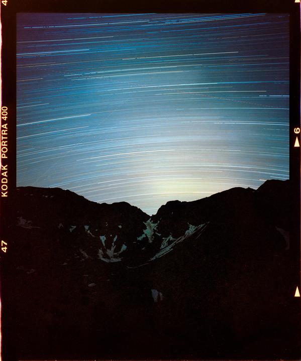 Star trails are visible above a dark mountain range at night.