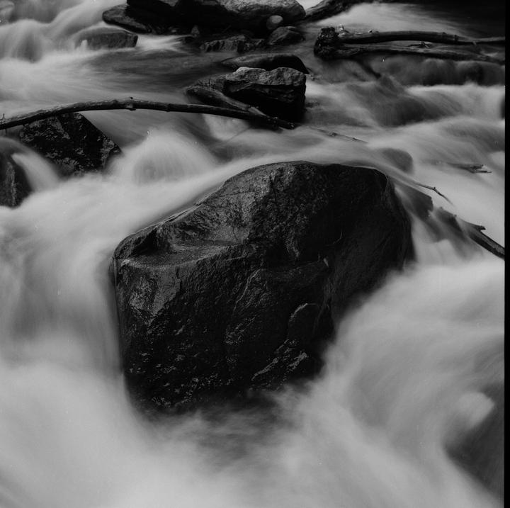 A large rock is surrounded by flowing water in a stream.