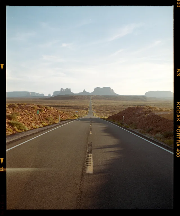 A long, straight road leads towards distant mesas under a bright sky.