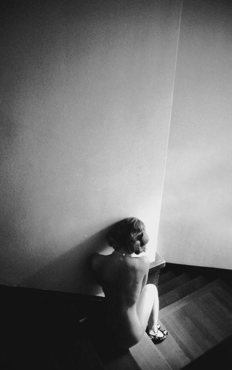 A woman with a pearl necklace sits on a wooden staircase with her back to the viewer.