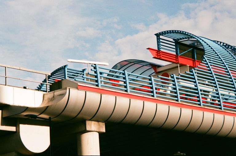 A modern building with blue railings and red accents is visible against a cloudy sky.
