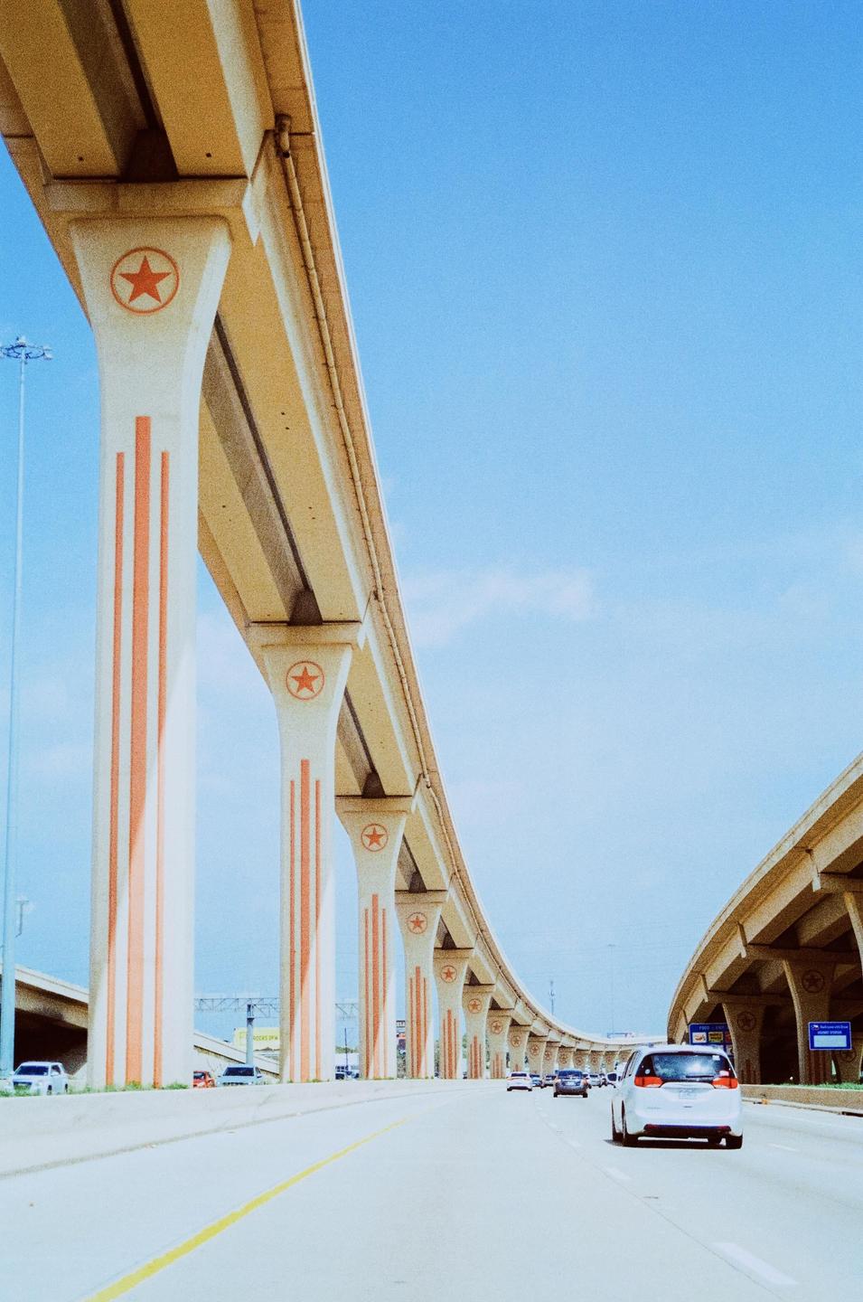 A highway with an elevated road supported by pillars decorated with stars is shown under a clear blue sky.