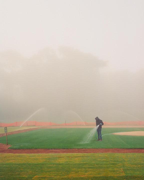 A man waters a baseball field on a foggy morning.