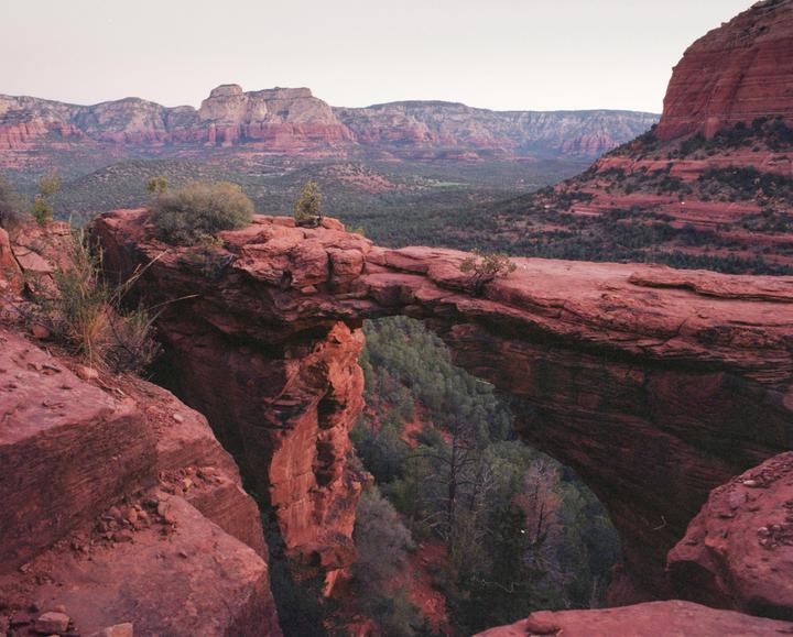 A natural rock arch spans a deep canyon with red rock mountains in the background.