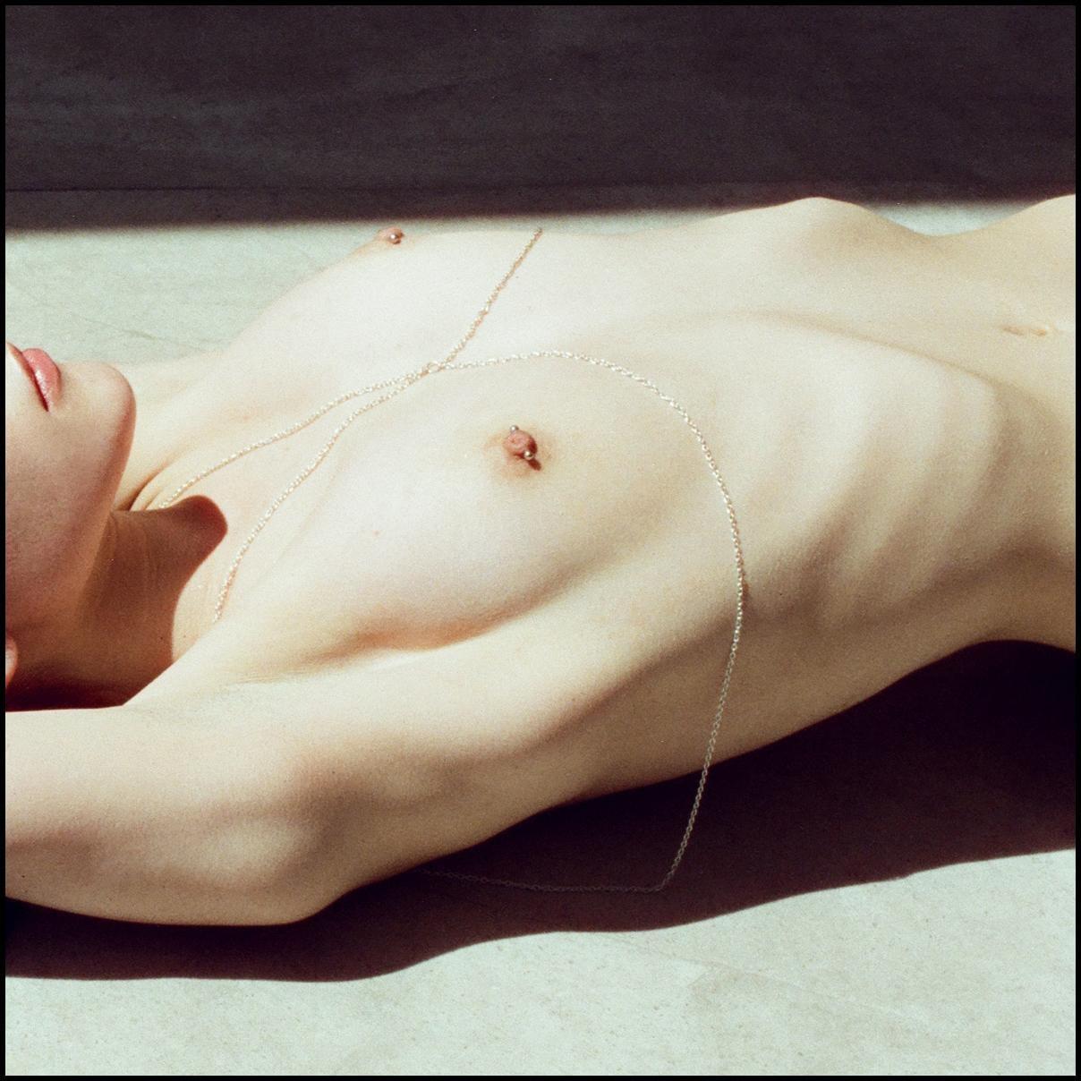 A woman lies on her back with a delicate chain draped across her chest.