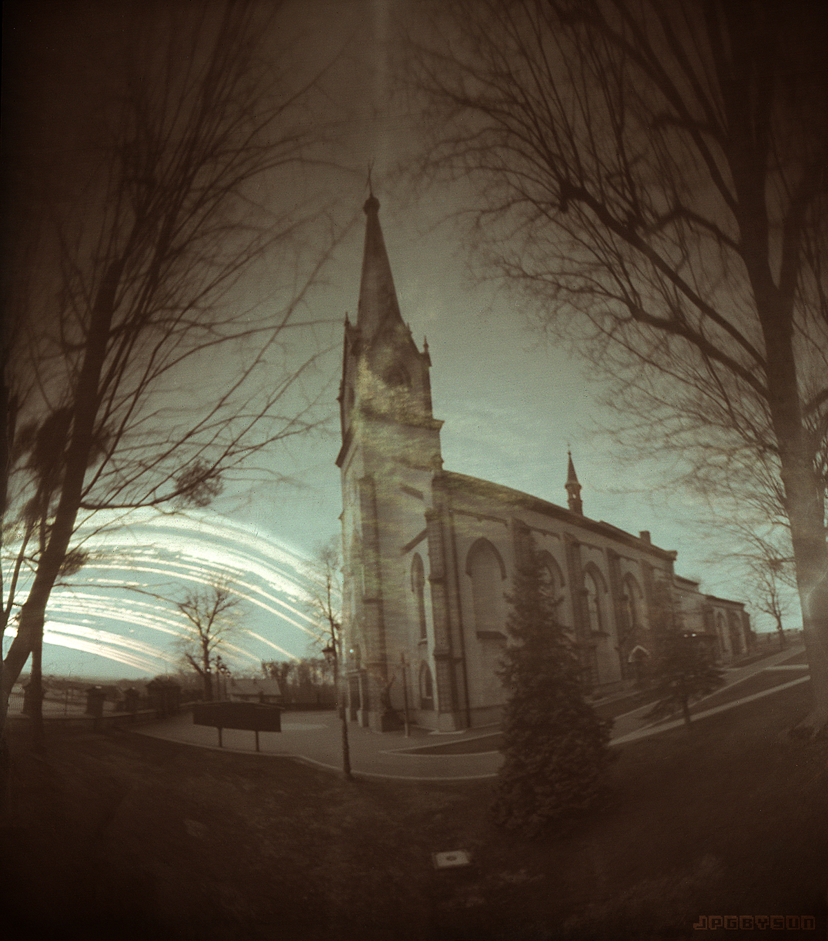 A church with a tall steeple is surrounded by bare trees under a light-streaked sky.