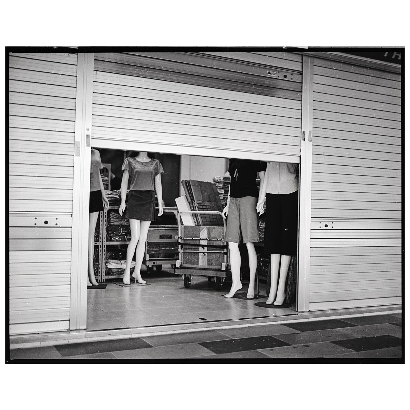 Several headless mannequins are visible behind a partially open metal roller shutter.
