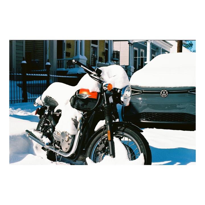 A motorcycle and a car are parked on a street covered in snow.