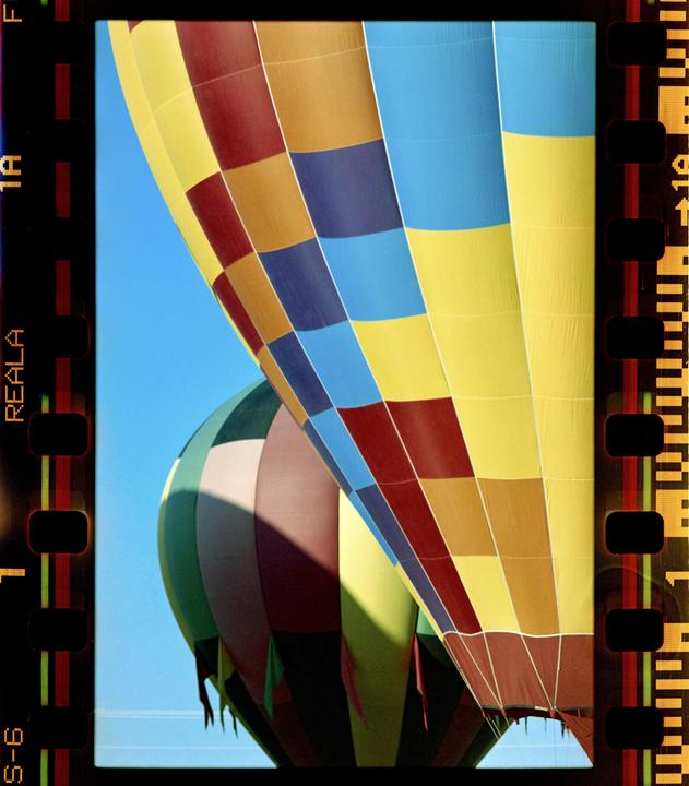Two hot air balloons with colorful checkered patterns are visible against a clear blue sky.