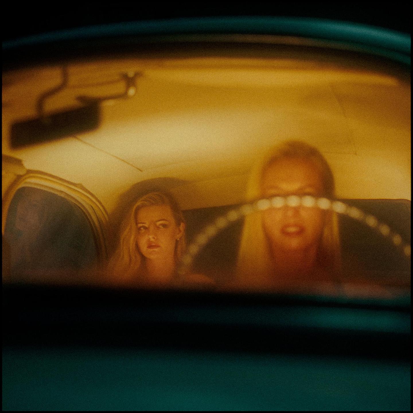 Two women are visible through the windshield of a car at night.