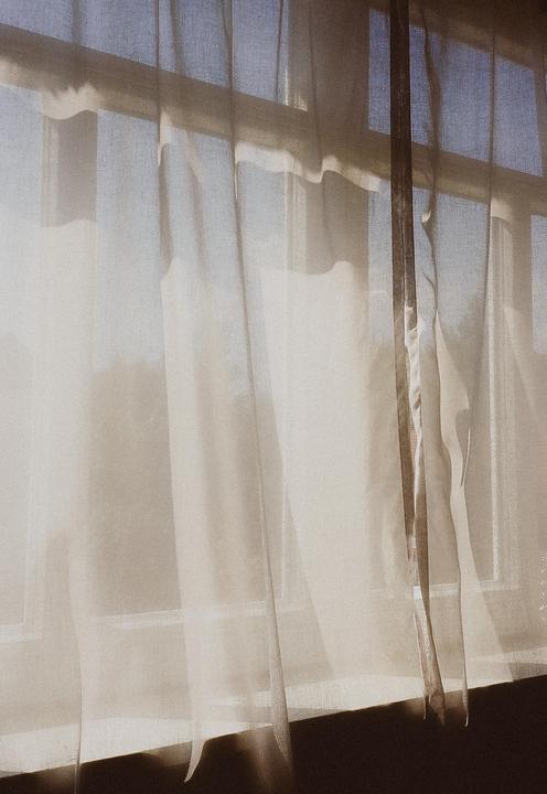 Sunlight streams through sheer white curtains covering a window.