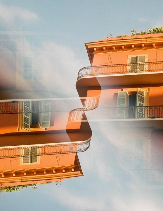 An orange building with balconies and windows is reflected and overlaid against a blue sky.