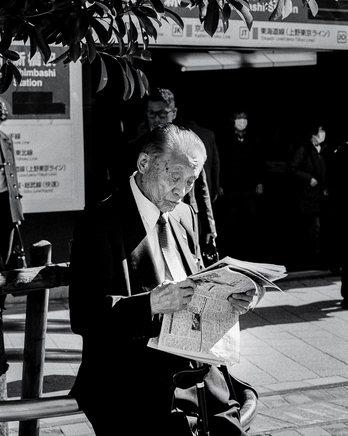 A man in a suit reads a newspaper on a street in Tokyo.