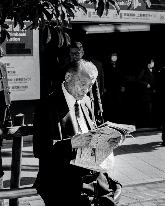 A man in a suit reads a newspaper on a street in Tokyo.