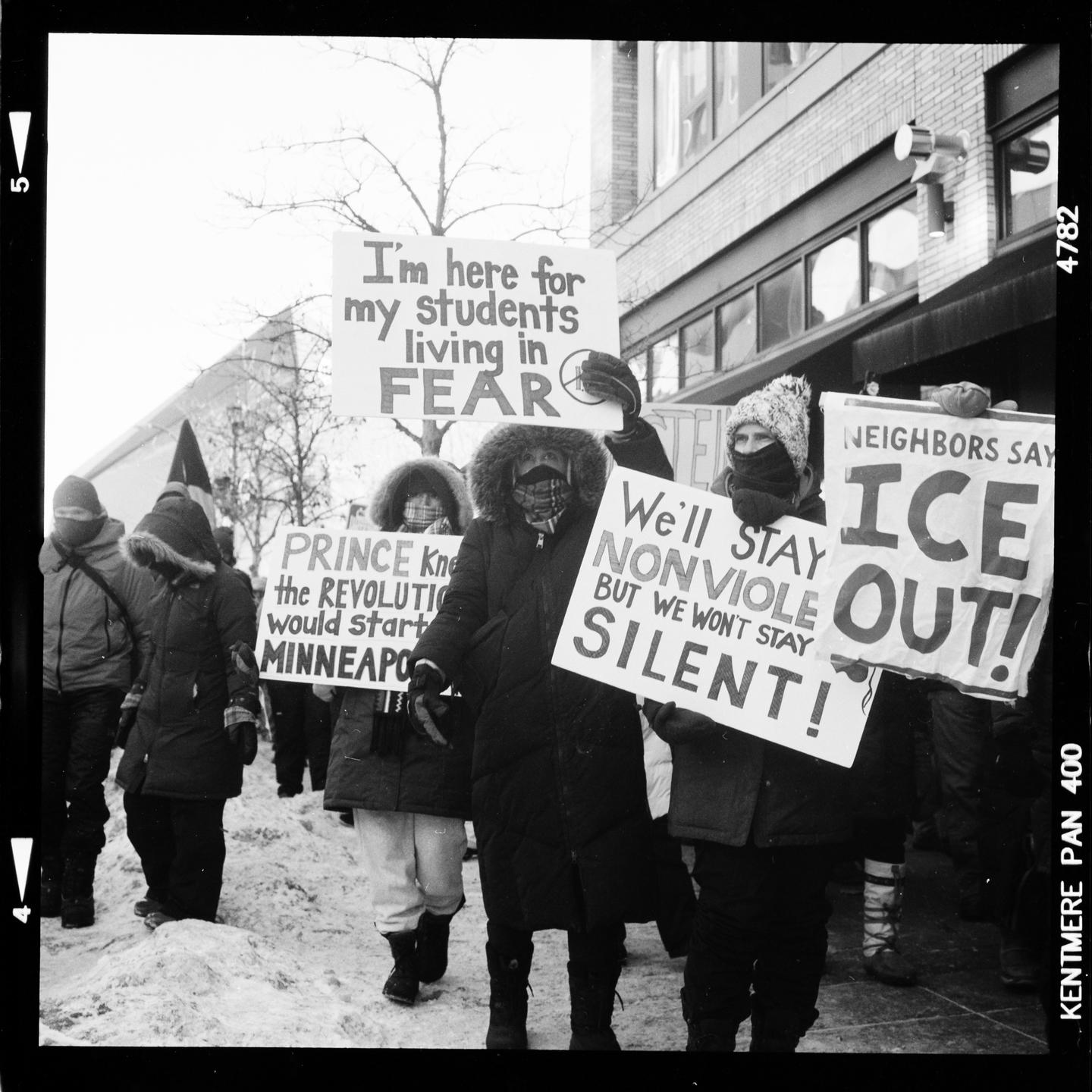 A group of people protest in the snow, holding signs with various messages.