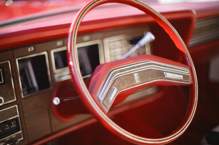 A red steering wheel and dashboard are visible inside a vintage car.