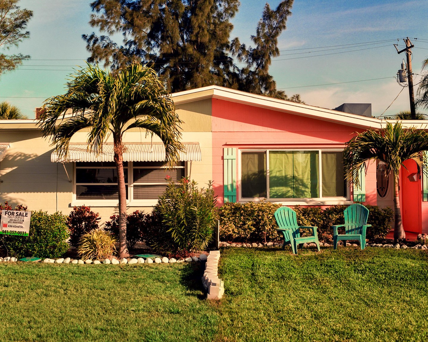 A pink and beige house with two green chairs in the front yard is seen under a blue sky.