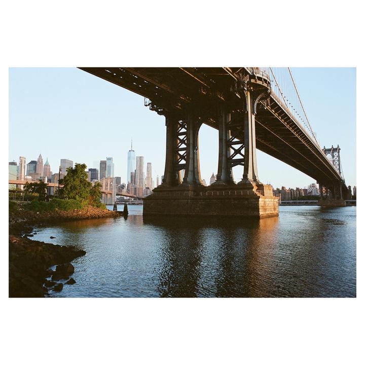 The Manhattan Bridge spans a body of water with a city skyline in the background.