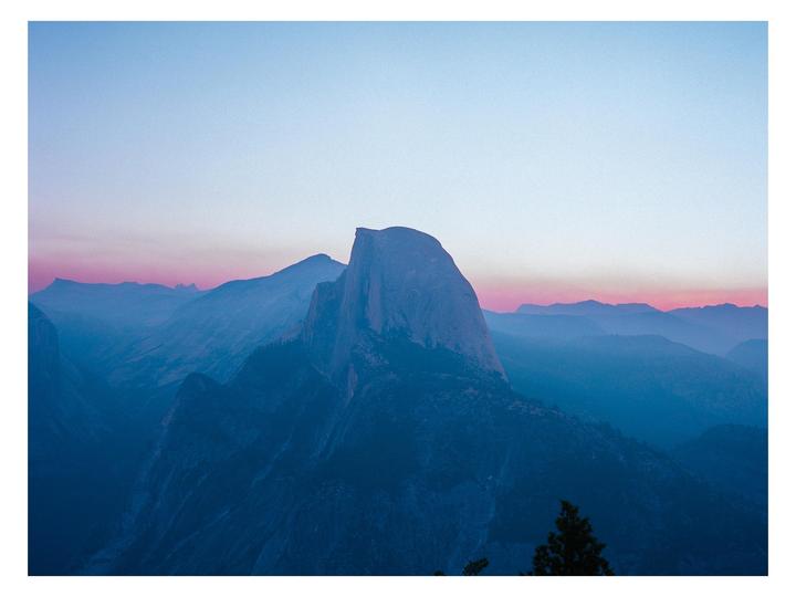 A sunrise over Half Dome shows a pink and blue sky above a mountain range.