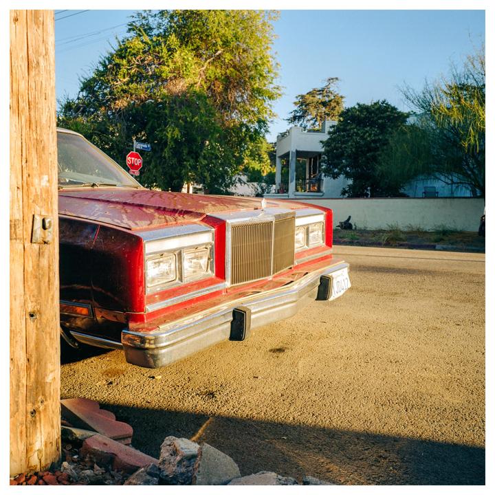 A red car is parked on a street next to a wooden post with a stop sign visible in the background.