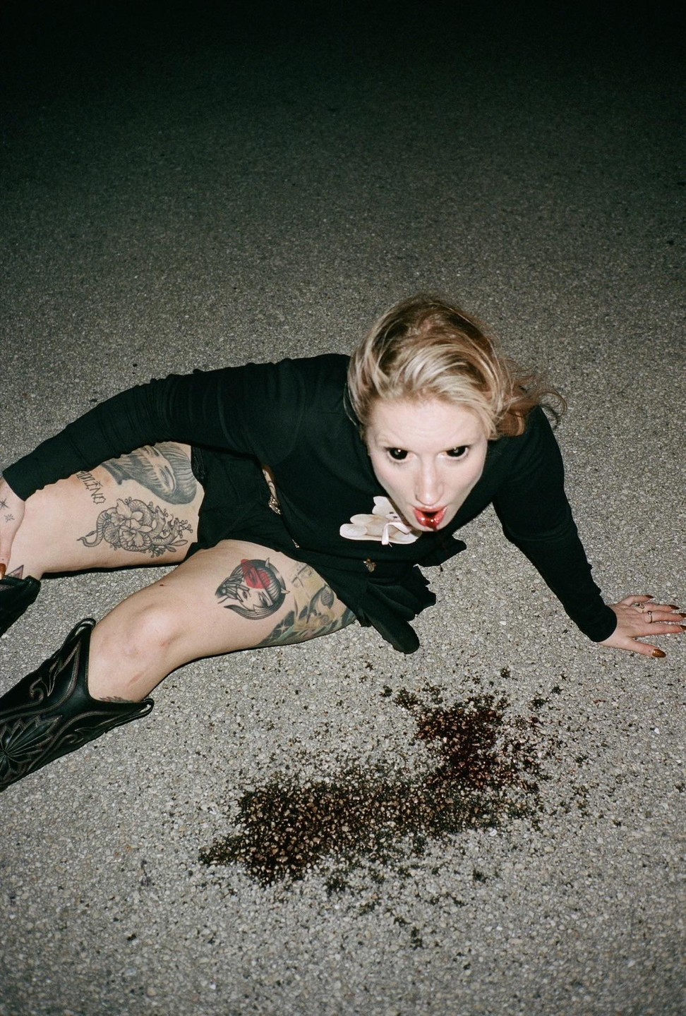 A woman with black eyes and blood on her mouth is on the ground next to a puddle of blood.