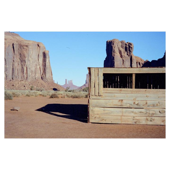 A wooden structure with a dark interior stands in a desert landscape with large rock formations under a clear sky.