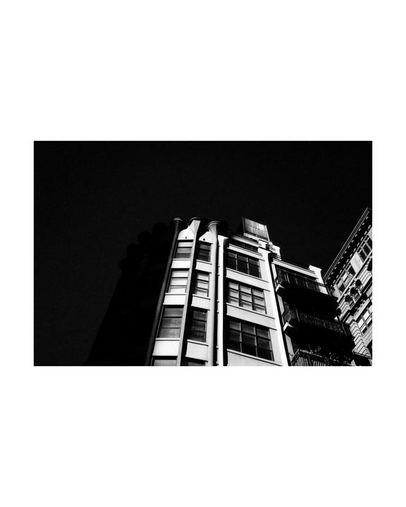 A low-angle view shows the facade of a tall building with many windows and balconies, with another building partially visible on the right.