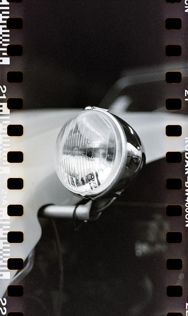 A close-up of a car headlight is visible with film borders on the left and right.