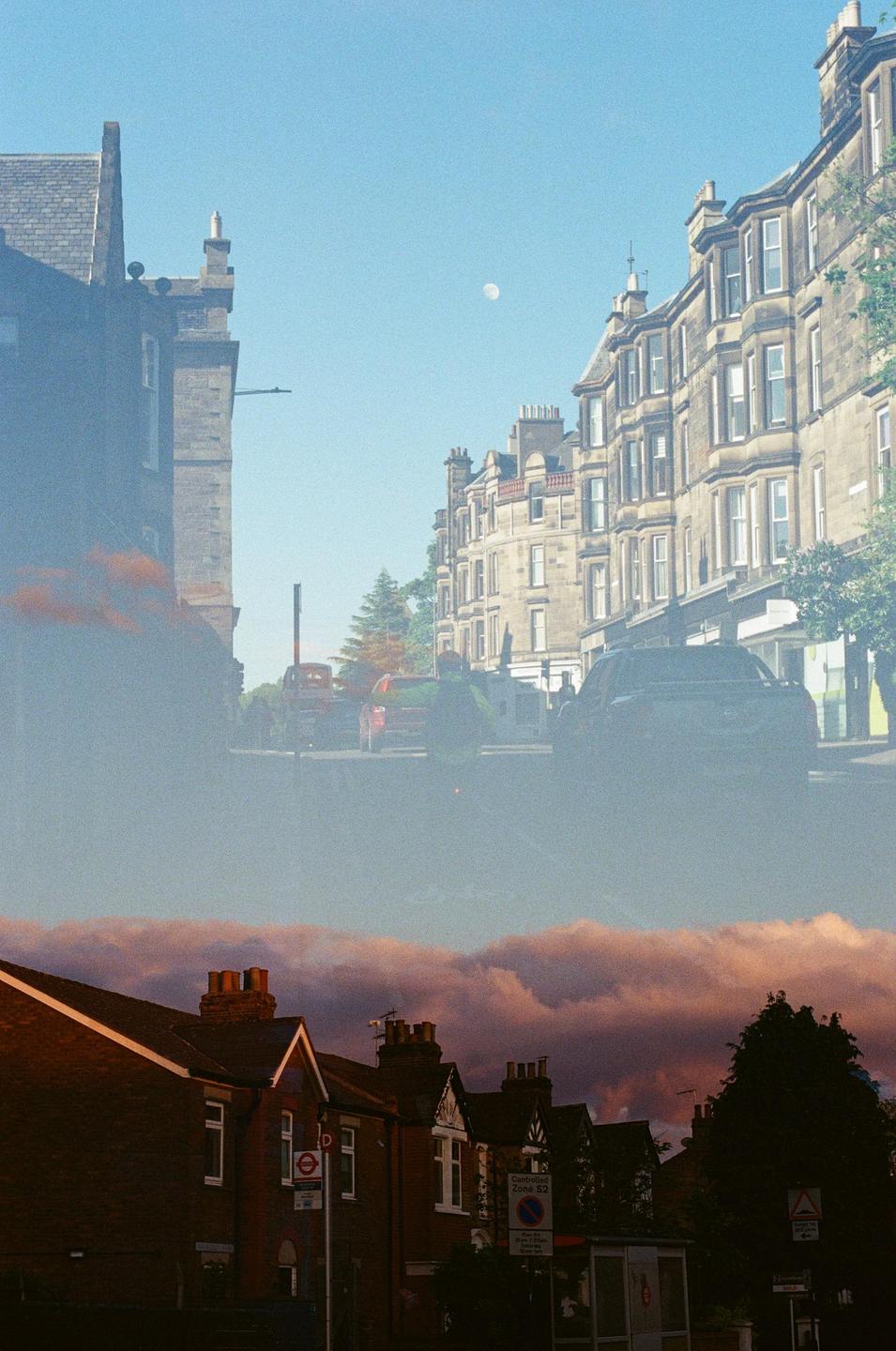 A double exposure shows a street with buildings and cars overlaid with a view of rooftops and clouds.