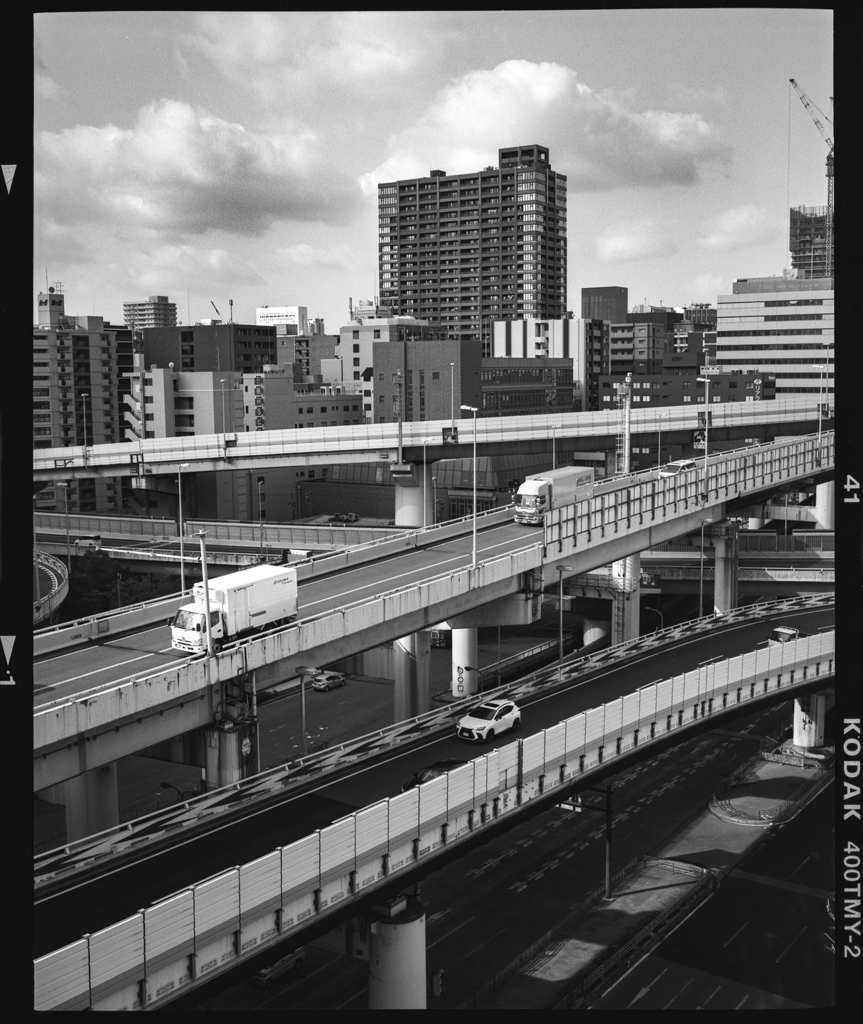 Multiple elevated highways with vehicles on them crisscross in front of a city skyline with a large building dominating the background.