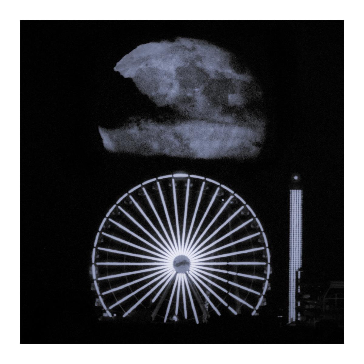 A large moon hangs above a brightly lit ferris wheel and a tall amusement park ride at night.