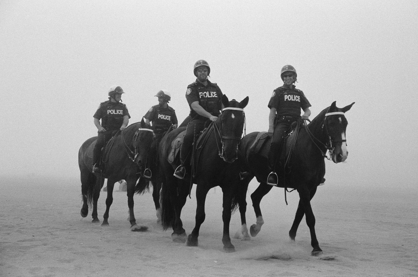 Four mounted police officers on horseback are visible in a hazy, monochrome setting.
