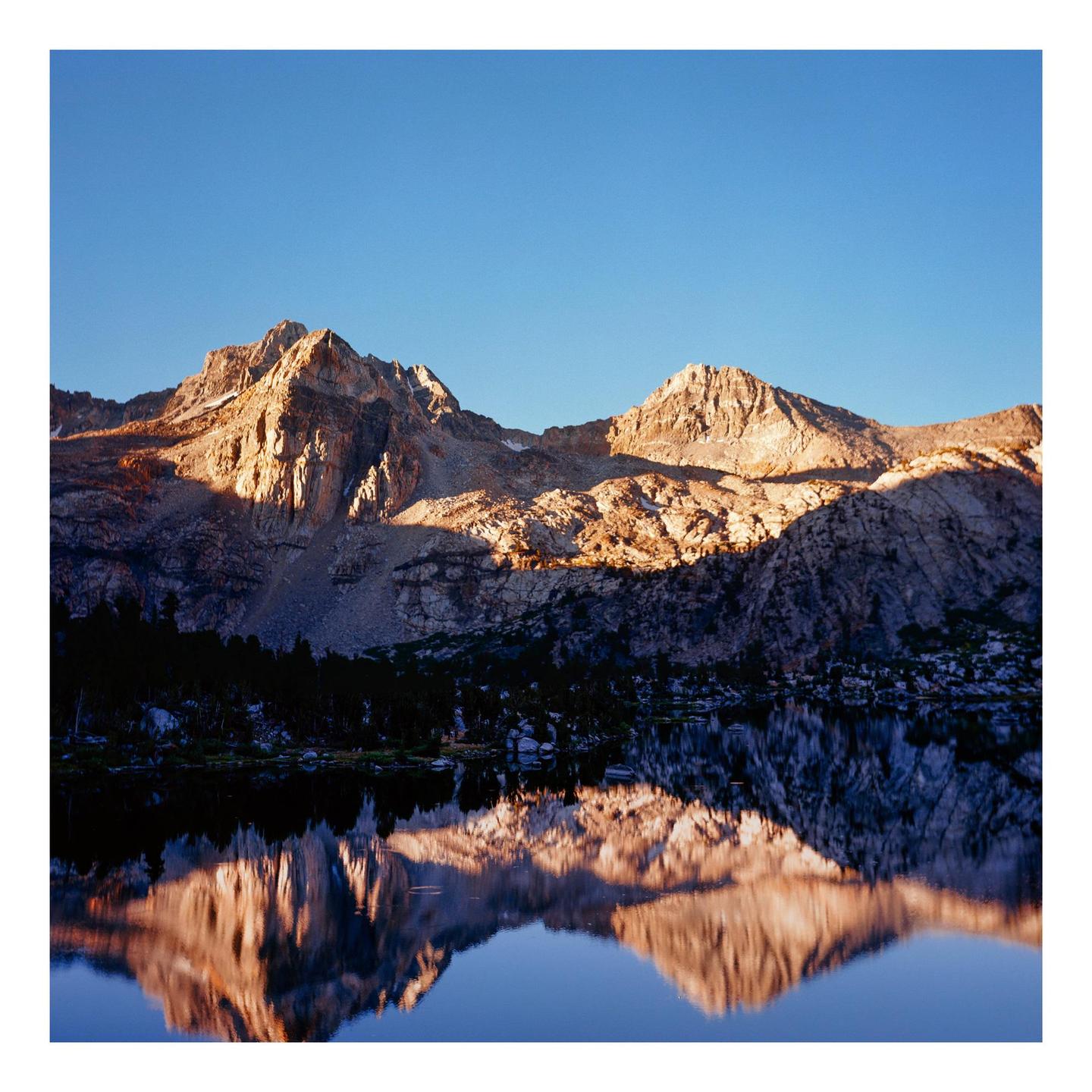 Mountains are reflected in a still lake under a clear sky.