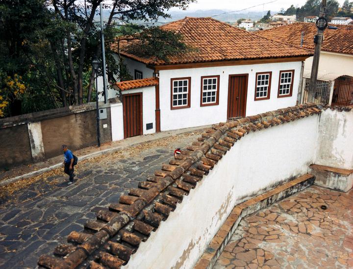 A man walks on a cobblestone street past a white building with a red tile roof.