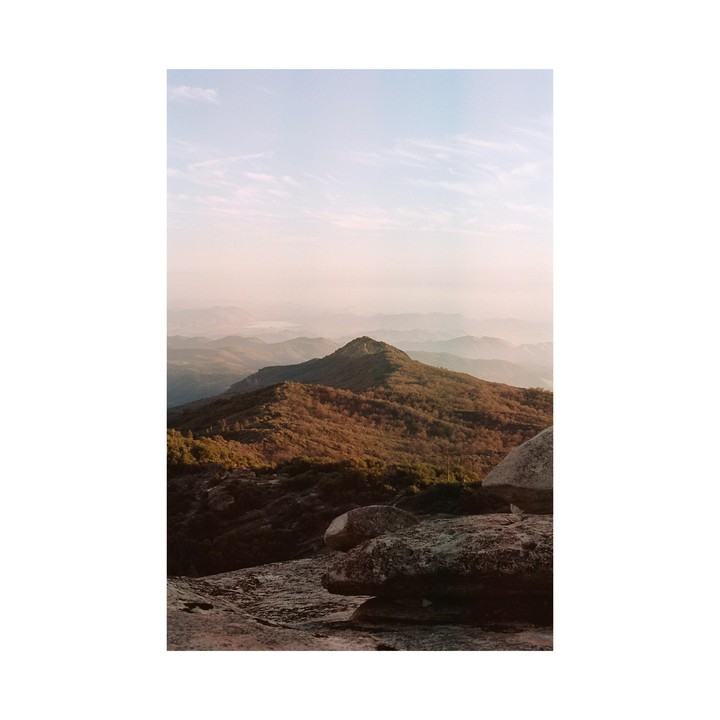 A mountain range with a prominent peak is visible under a hazy sky, with large rocks in the foreground.