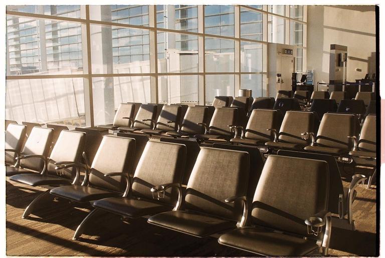 Rows of empty airport seats are illuminated by sunlight streaming through large windows.