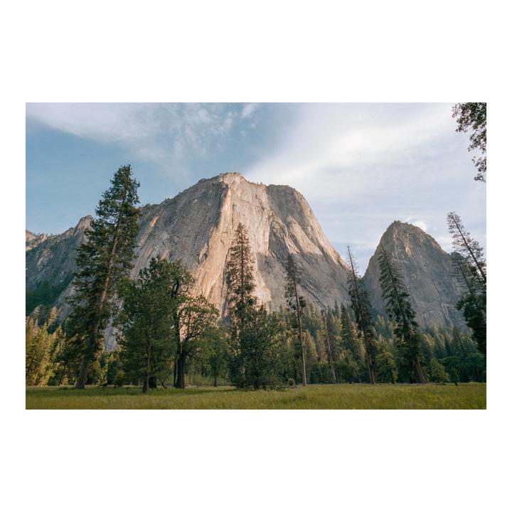A wide shot shows a valley with a large mountain and many trees.