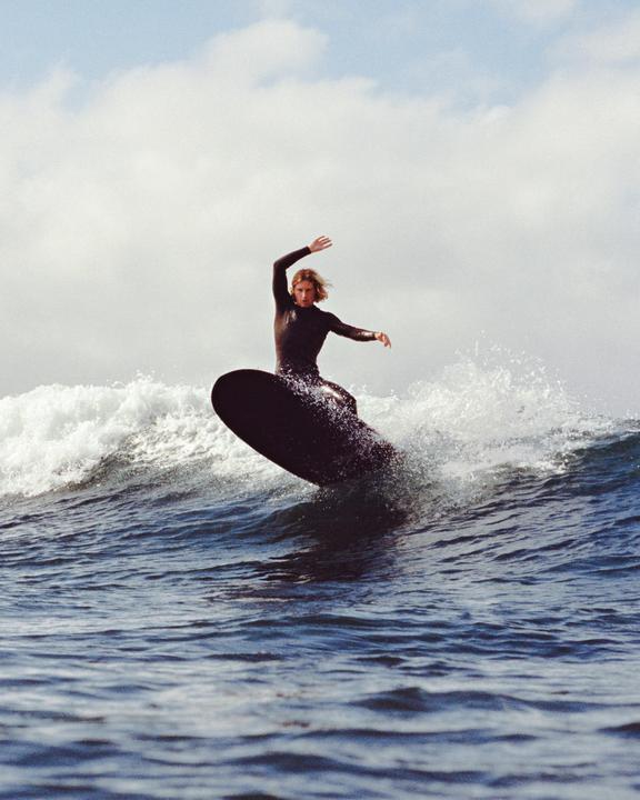 A man in a wetsuit surfs a wave on a dark surfboard.