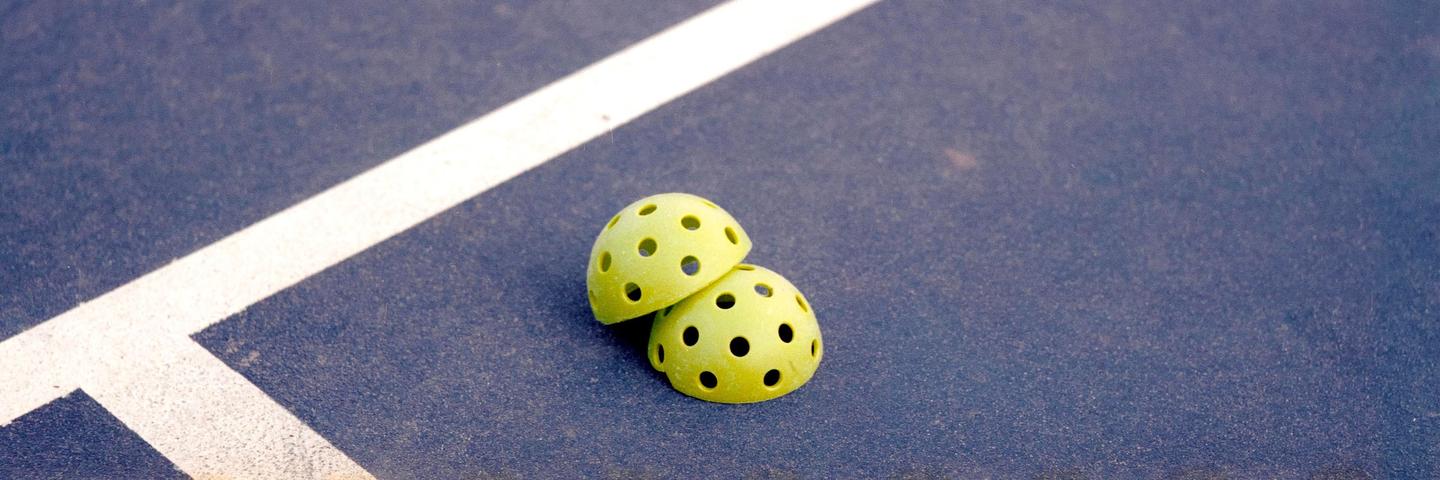 Two yellow pickleball halves are resting on a blue court next to a white line.