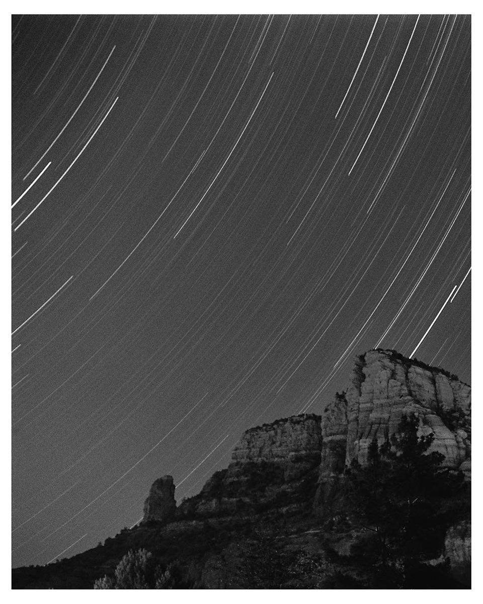 Star trails streak across the night sky above a rugged mountain landscape.