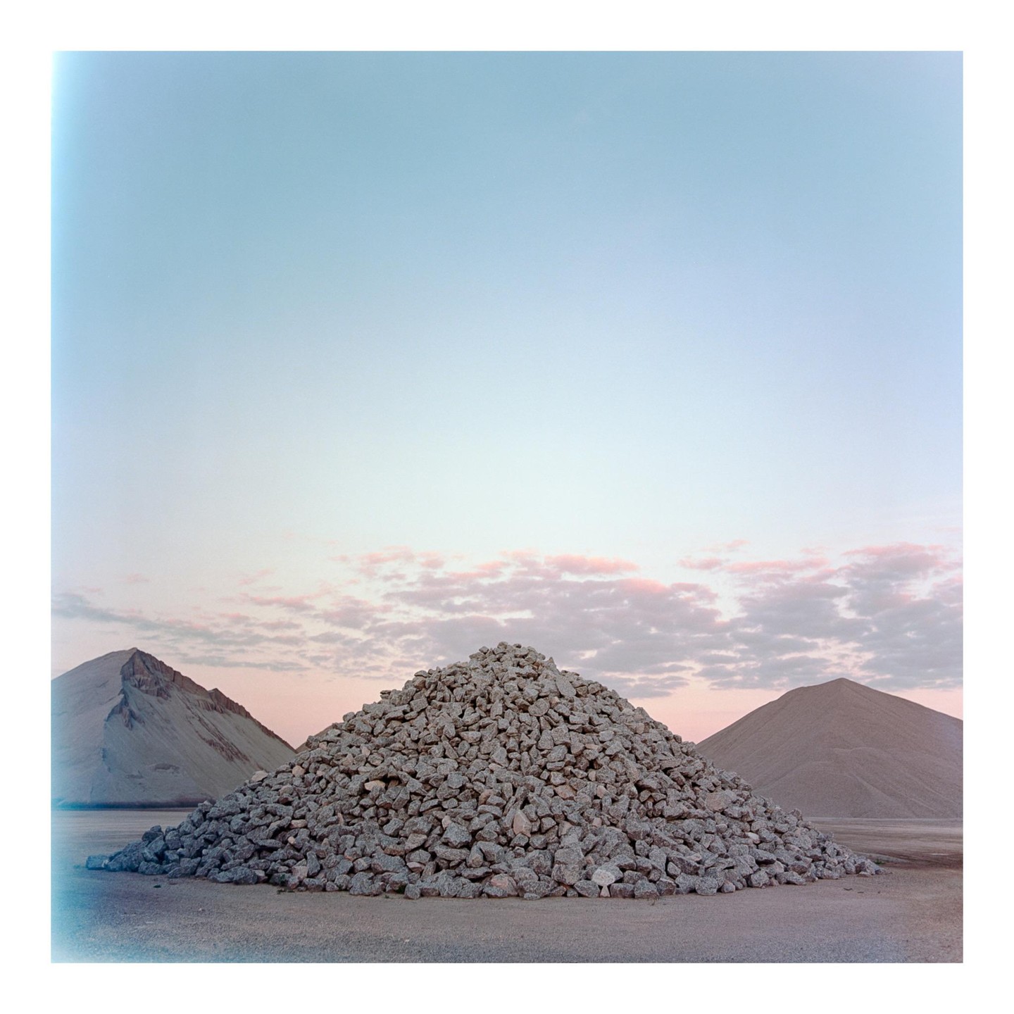A large mound of gravel sits in the foreground with two smaller mounds behind it under a sky with pink clouds.